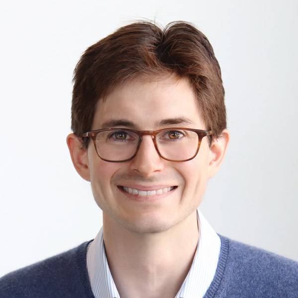 Headshot of Matthew Spitzer, PhD. He is facing the camera and smiling. He is wearing brown rimmed glasses and a blue blazer with a white dress shirt underneath. He is standing in front of a plain white background.